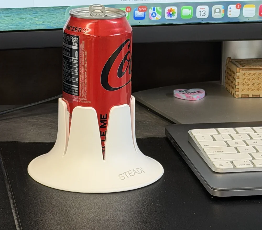 A standard Coca-Cola can fitted in White Steadi on a desk mat beside a keyboard; the whole flared base is visible